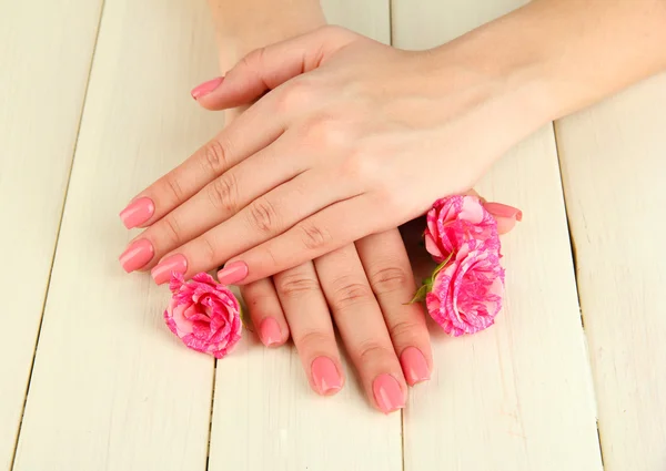 Manos de mujer con manicura rosa y flores, sobre fondo de madera —  Fotos de Stock