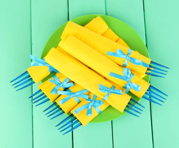Modré plastové příbory zabalený do žluté papírové ubrousky, na barevné dřevěné pozadí — Stock fotografie