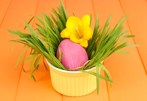 Ovo de Páscoa na tigela com grama na mesa de madeira laranja de perto — Fotografia de Stock