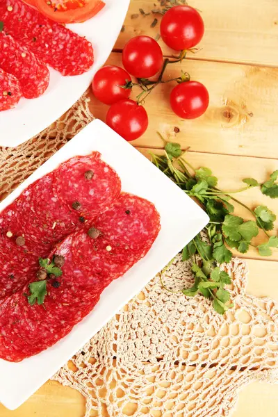 Leckere Salami auf Tellern auf Holztisch in Großaufnahme — Stockfoto