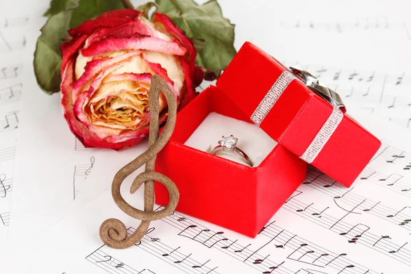 Σολ, τριαντάφυλλο και πλαίσιο κρατώντας το γαμήλιο δαχτυλίδι στο μουσικό υπόβαθρο — Φωτογραφία Αρχείου