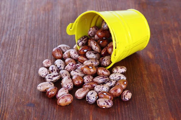 Gekanteld emmer met bonen op houten achtergrond — Stockfoto