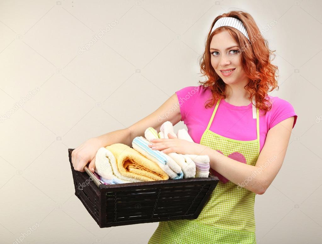 Housewife carrying laundry basket full of clothing on grey background