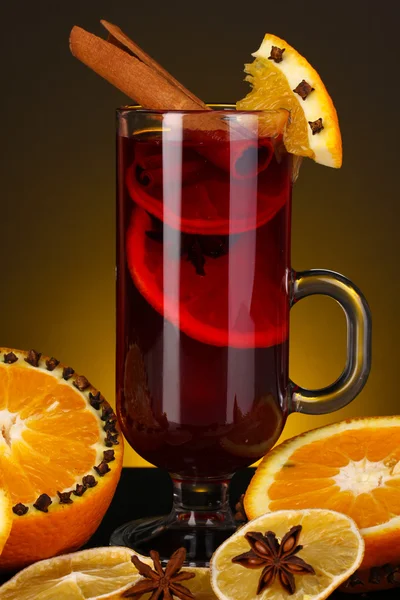 Duftender Glühwein im Glas mit Gewürzen und Orangen auf gelbem Hintergrund — Stockfoto