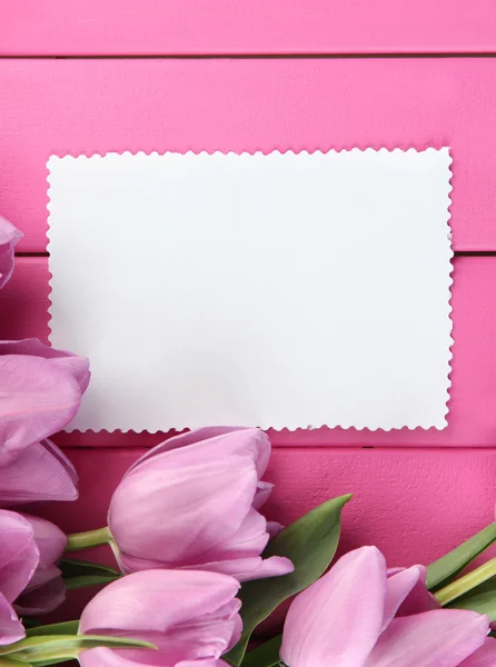 束美丽的紫色郁金香和粉红色的木制背景上的空白卡 — 图库照片