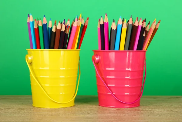 Kleurrijke potloden in twee emmers op tafel op groene achtergrond — Stockfoto