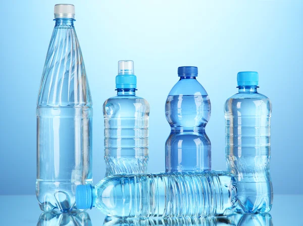 Diferentes garrafas de água no fundo azul — Fotografia de Stock