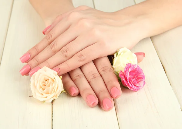 Frauenhände mit rosa Maniküre und Blumen, auf hölzernem Hintergrund — Stockfoto