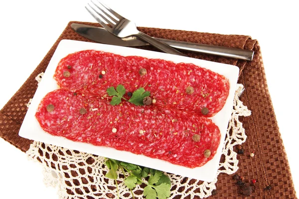 Tasty salami on plate on napkin isolated on white — Stock Photo, Image