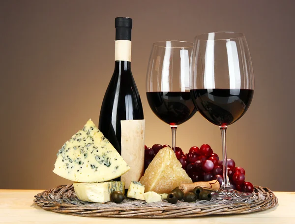 Refined still life of wine, cheese and grapes on wicker tray on wooden table on beige background — Stock Photo, Image