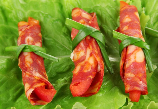 Salami rolls on green salad leaves, close up — Stock Photo, Image