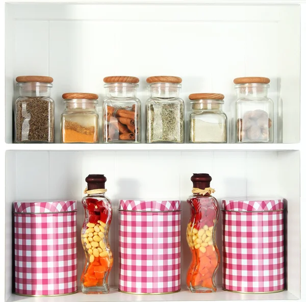 Beautiful white shelves with spices in glass bottles — Stock Photo, Image