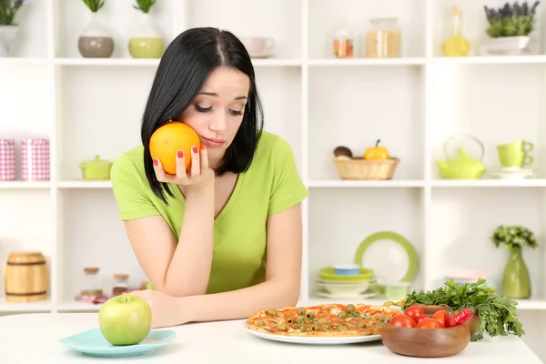 Mooi meisje selecteert pizza of dieet op keuken achtergrond — Stockfoto