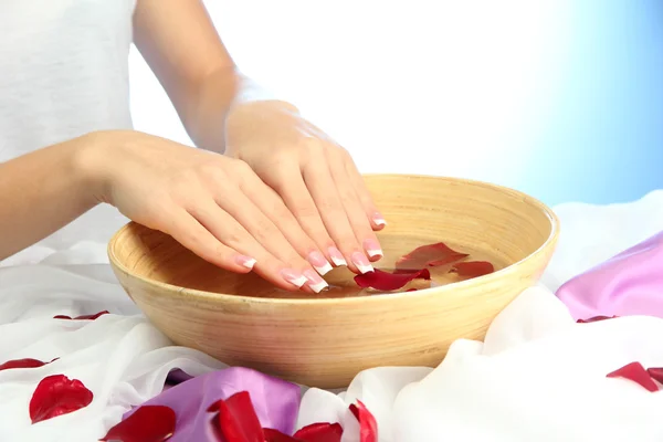 Mani di donna con ciotola di legno di acqua con petali, su sfondo blu — Foto Stock