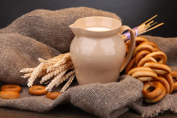 Jar of milk, tasty bagels and spikelets on wooden table, on grey background — Stock Photo, Image