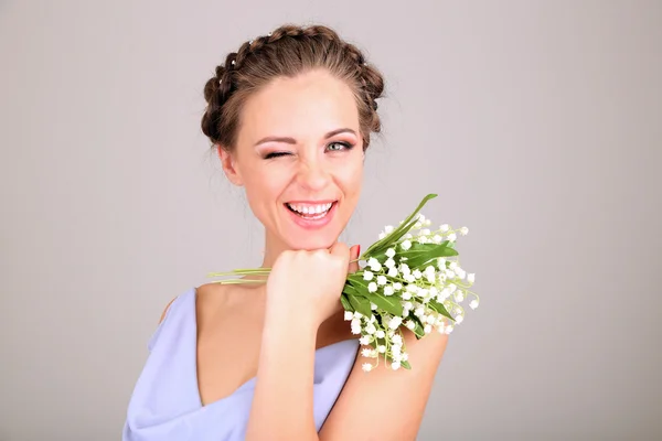 Mujer joven con hermoso peinado y flores, sobre fondo gris — Foto de Stock