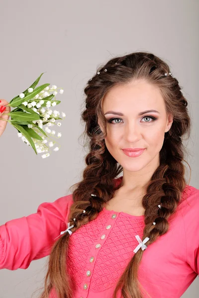 Ung kvinne med vakker frisyre og blomster, på grå bakgrunn – stockfoto