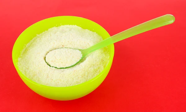 Powdered milk in bowl for baby and spoon on red background — Stock Photo, Image