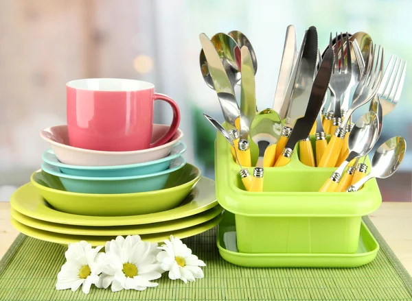 Piatti, forchette, coltelli, cucchiai e altri utensili da cucina su tappetino di bambù, su sfondo brillante — Foto Stock