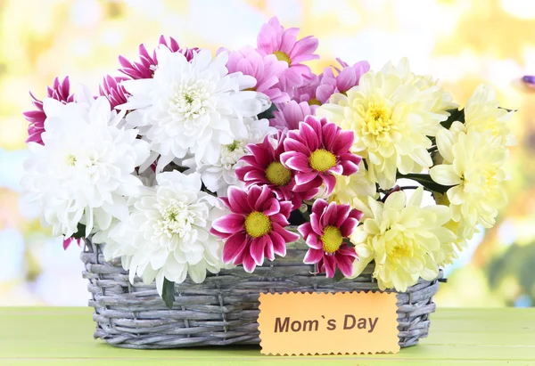 Букет красивых хризантем в плетеной корзине на столе на ярком фоне — стоковое фото