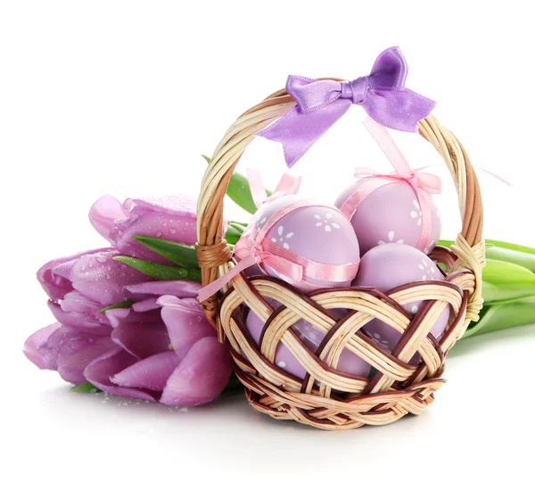Huevos de Pascua brillantes en cesta y tulipanes, aislados en blanco — Foto de Stock