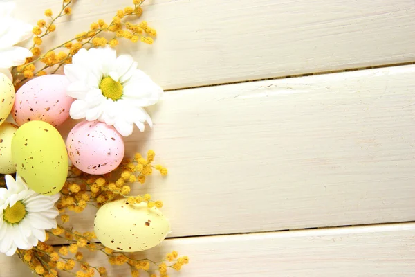 Huevos de Pascua y flores de mimosa, sobre fondo de madera blanca — Foto de Stock