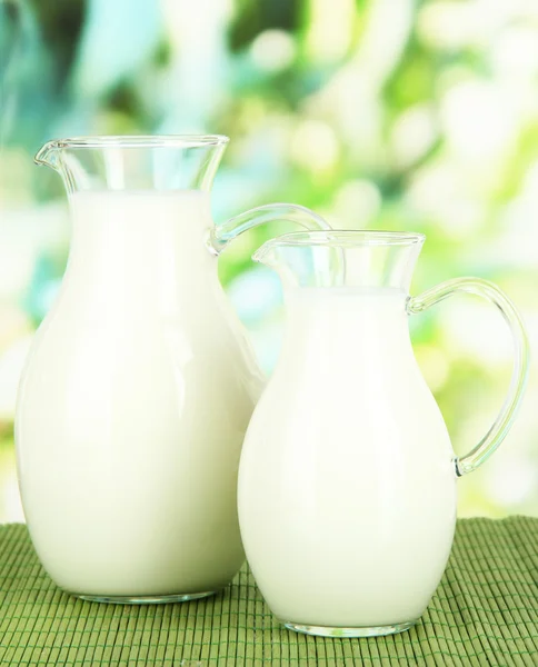 Pitchers of milk on table on bright background — Stock Photo, Image