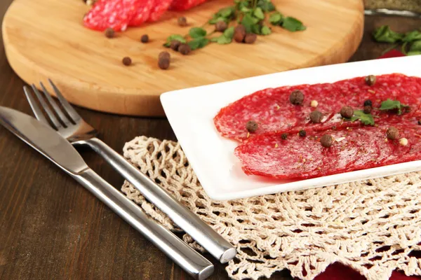 Välsmakande salami på plattan och styrelsen på träbord närbild — Stockfoto