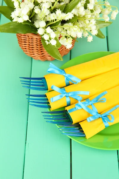 Garfos de plástico azul envolto em guardanapos de papel amarelo, na cor de fundo de madeira — Fotografia de Stock