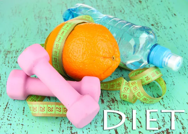 Orange with measuring tape, dumbbells and bottle of water, on color wooden background — Stock Photo, Image