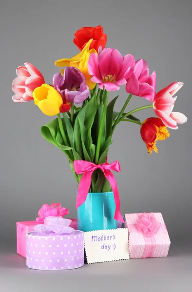 Красивые тюльпаны в букете с подарками и запиской на сером фоне — стоковое фото