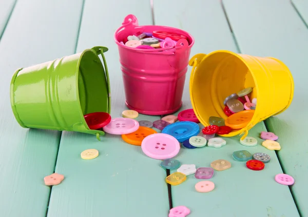 Colorful buttons strewn from buckets on wooden background — Stock Photo, Image