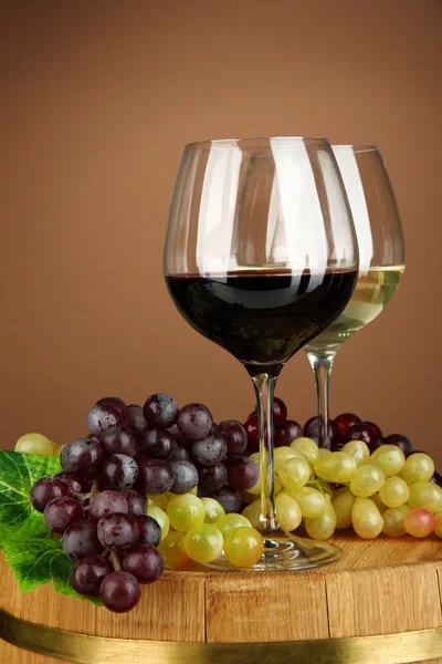 Glasses of red and white wine, grape on wooden barrel, on color background — Stock Photo, Image