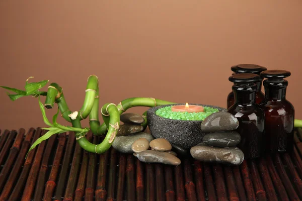 Still life with green bamboo plant and stones, on bamboo mat on color background — Stock Photo, Image