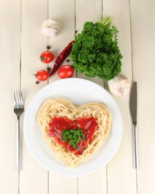 Cooked spaghetti carefully arranged in heart shape and topped with tomato sauce, on wooden background