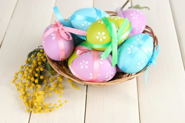 Beyaz ahşap zemin üzerinde sepet ve Mimoza çıtır Paskalya yumurtaları