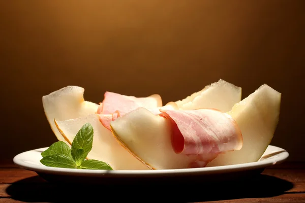 Parma ham and melon, on wooden table, on brown background — Stock Photo, Image