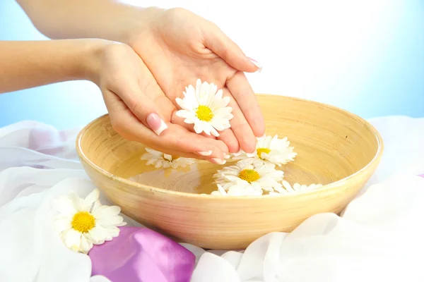 Manos de mujer con cuenco de madera de agua con flores, sobre fondo azul — Foto de Stock