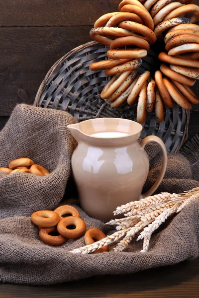 Баночка молока, смачні бублики та колоски на дерев'яному фоні — стокове фото