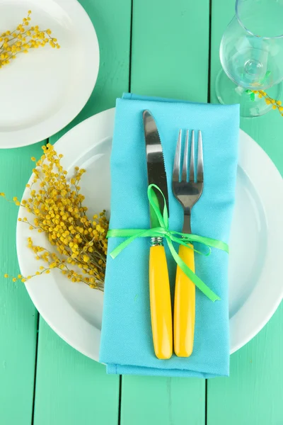 Нож и вилка, завернутые в салфетку, на тарелке, на цветном деревянном фоне — стоковое фото