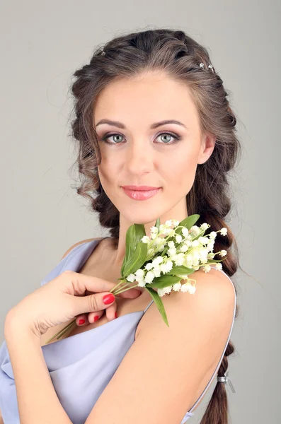 Ung kvinna med vackra frisyr och blommor, på grå bakgrund — Stockfoto