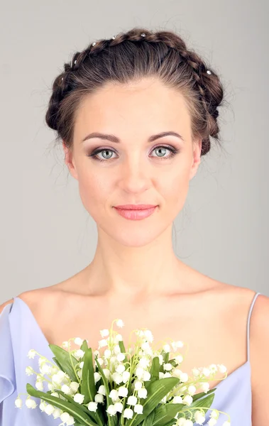 Mujer joven con hermoso peinado y flores, sobre fondo gris — Foto de Stock