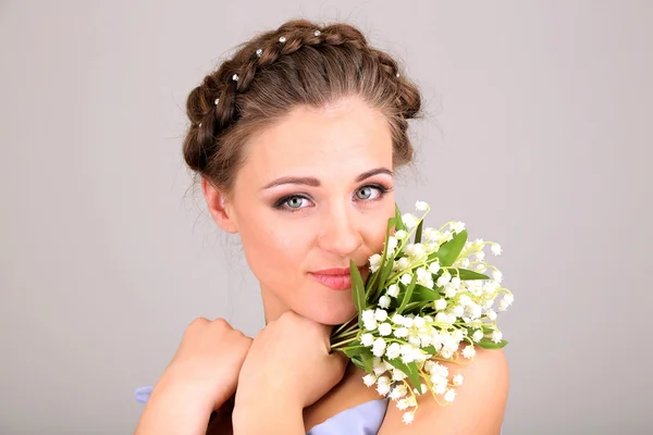 Mladá žena s krásný účes a květiny, na šedém pozadí — Stock fotografie