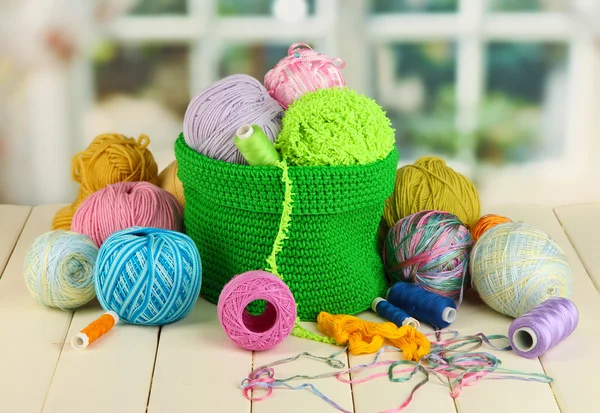 Colorful yarn for knitting in green basket on wooden table on window background — Stock Photo, Image