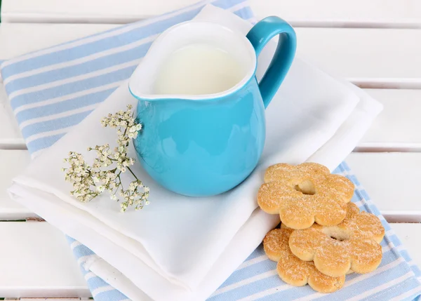 Blue jug with milk and cookies on wooden picnic table close-up — Stock Photo, Image