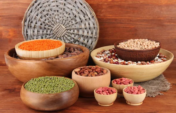 Různé druhy fazolí v miskách na dřevěné pozadí — Stock fotografie