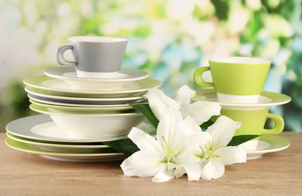 Empty plates and cups on wooden table on green background — Stock Photo, Image