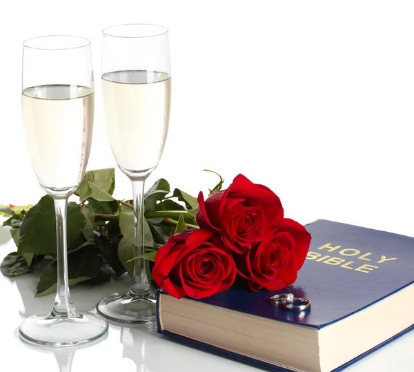 Anelli nuziali sulla bibbia con rose e bicchieri di champagne isolati su bianco — Foto Stock