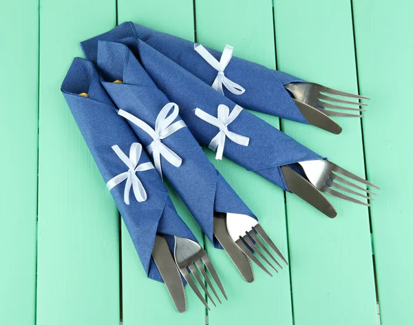 Forks and knives wrapped in blue paper napkins, on color wooden background — Stock Photo, Image