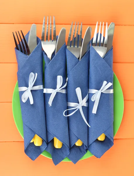 包裹在蓝色纸餐巾，彩色木制背景上的刀子和叉子 — 图库照片